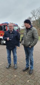 Weihnachtsbaumschmücken Foto: Goedecke Zwei Männer mit Glühweinbechern vor dem Feuerwehrauto unterhalten sich.