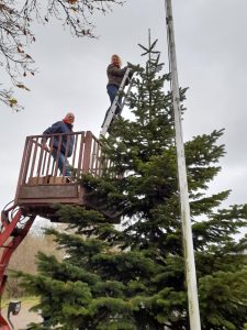 Weihnachtsbaumschmücken Foto: Jutta Boldt Birgit Johannsen und Carsten Andresen im Hubwagen oben an der Tannenbaumspitze lächeln in die Kamera.