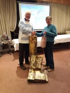 Sie sehen Joachim Spengler und Birgit Kiehn-Schmeling bei der Übergabe eine Geschenkes. Im Vordergrund alte Schiffsteile der Feuerland.
