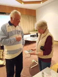 Sie sehen einen Mann und eine Frau, die sich ein Buch anschauen. Im Hintergrund Videoequippment.