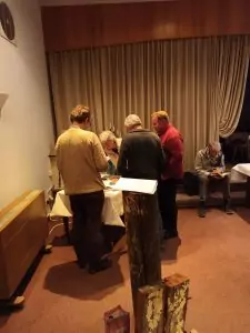 Sie sehen fünf Menschen an eienm Tisch stehend. Im Vordergrund Schiffsreste des Schiffes Feuerland.