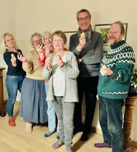 Sie sehen zwei Männer und vier Frauen mit Holzostereiern in der Hand in die Kamera lächeln.