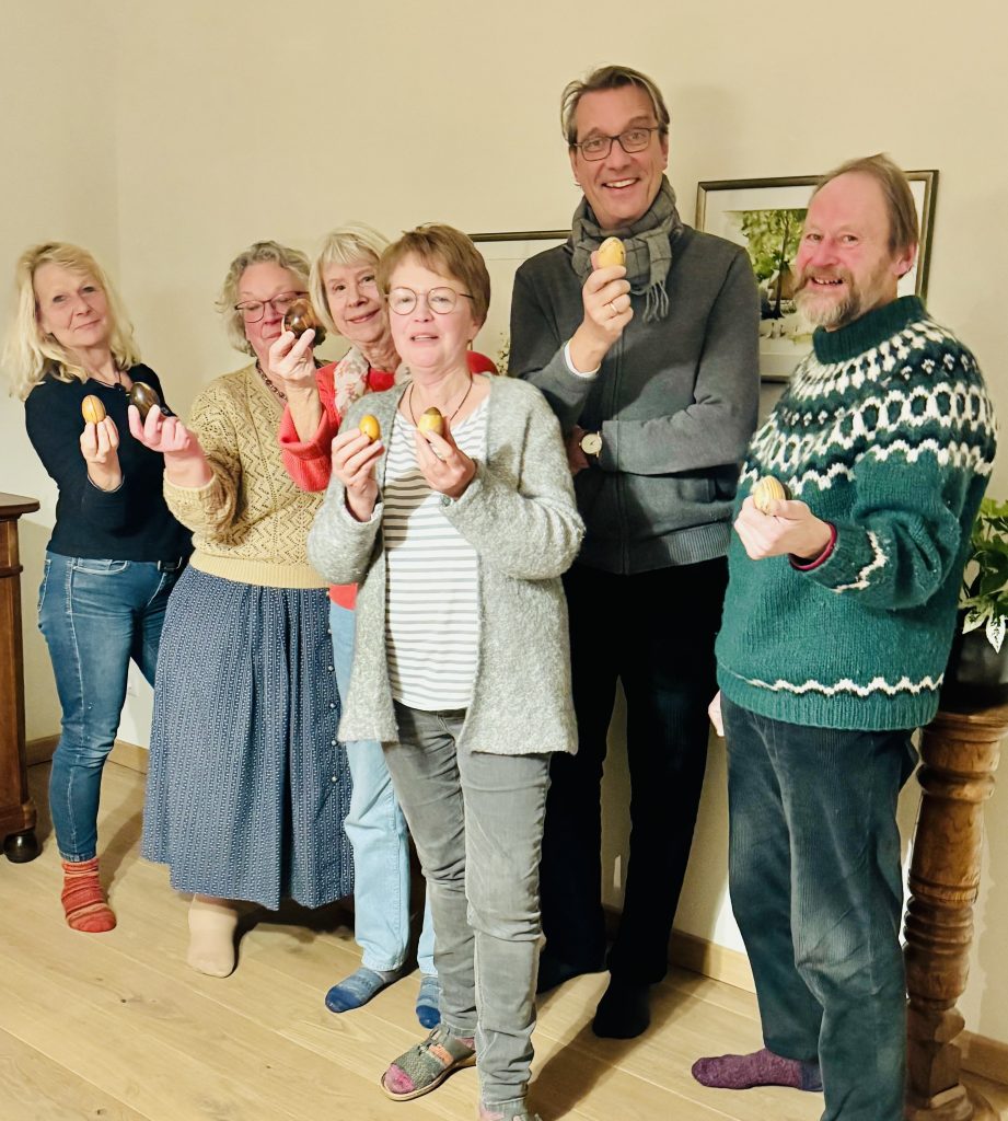 Sie sehen zwei Männer und vier Frauen mit Holzostereiern in der Hand in die Kamera lächeln.